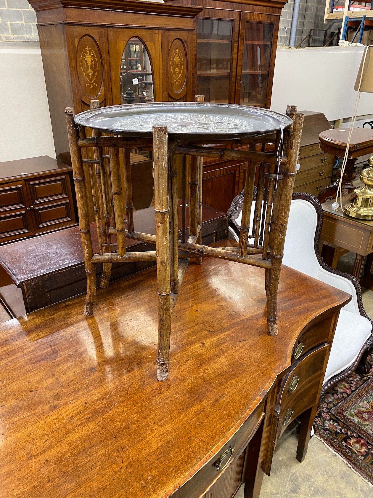 An early 20th century circular embossed copper tray on bamboo folding frame, diameter 58cm, height 67cm.